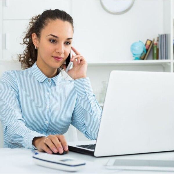Woman on cell phone at desk behind a laptop