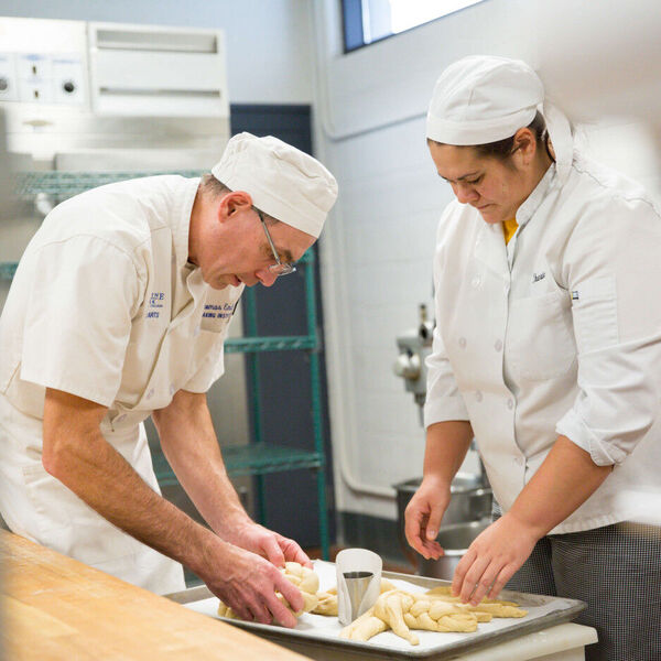 Two chefs making pastries in white coats and chef hats