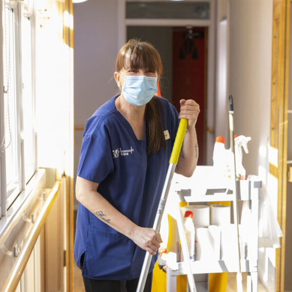 Person with mask mopping hardwood with cleaning cart behind them